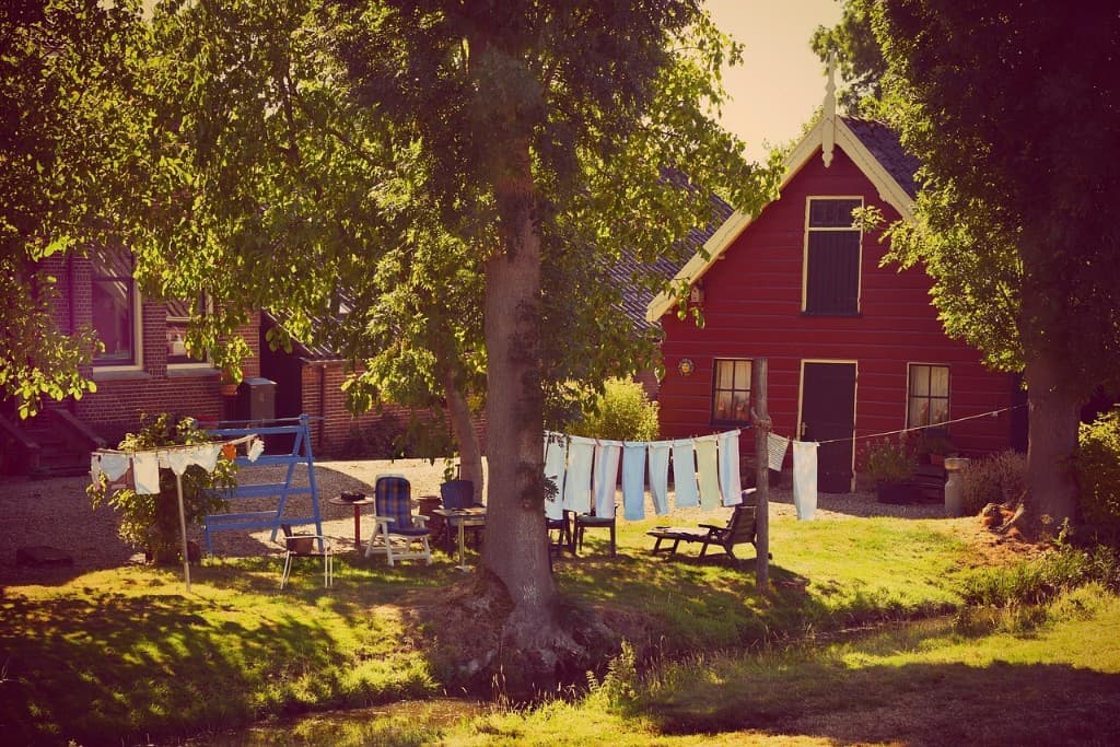 Röd svensk gårdsbyggnad en sommarkväll med tvätt på tork mellan lummiga träd.